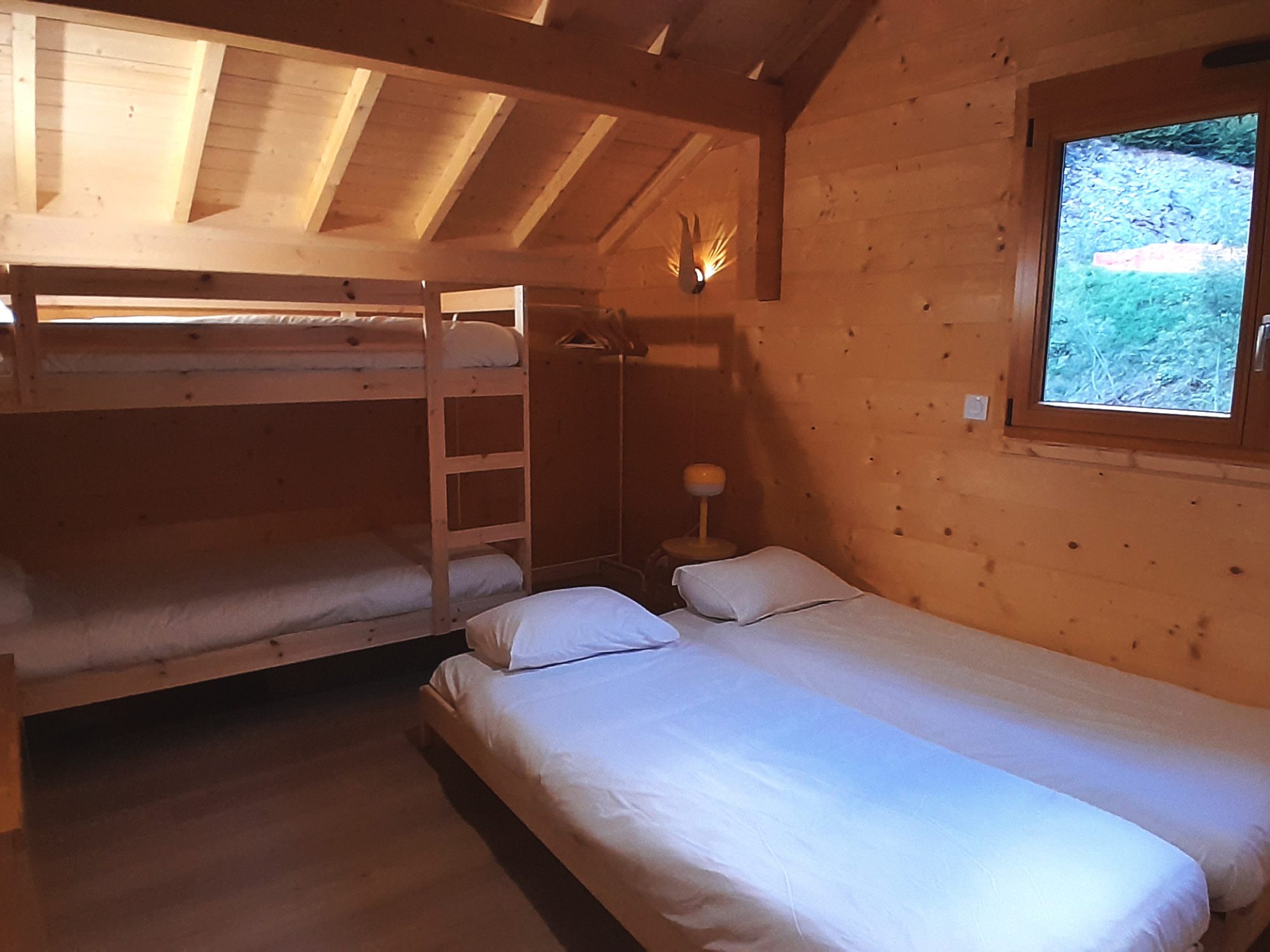 Dortoir avec 4 lits dont 2 lits superposés au chalet La Godille, location en Savoie. Mobilier et murs en bois, lits confortables, draps fournis.