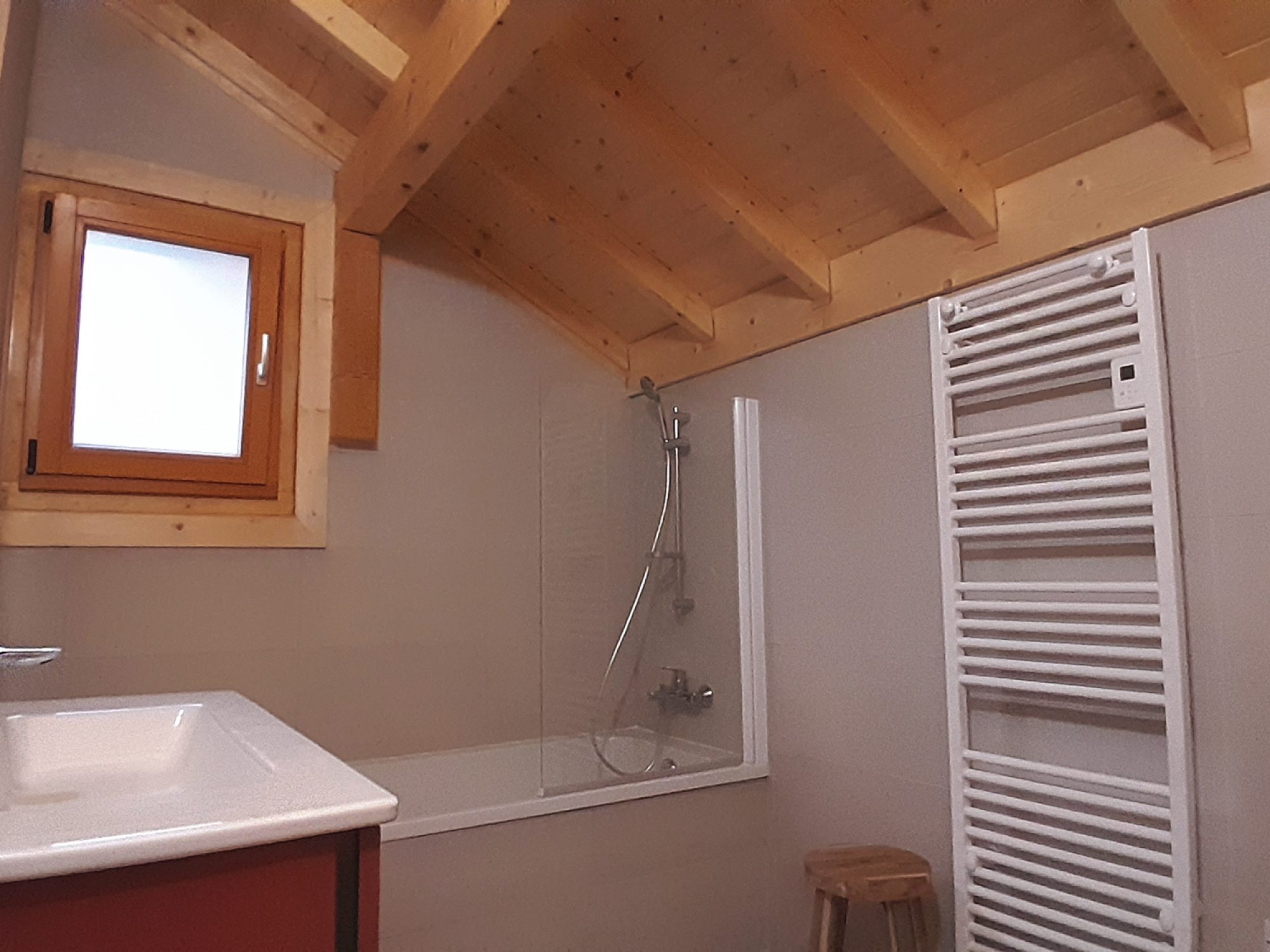 Salle de bain de l'étage du chalet La Godille, location en Savoie. Tons terracotta et gris, plafond en bois.