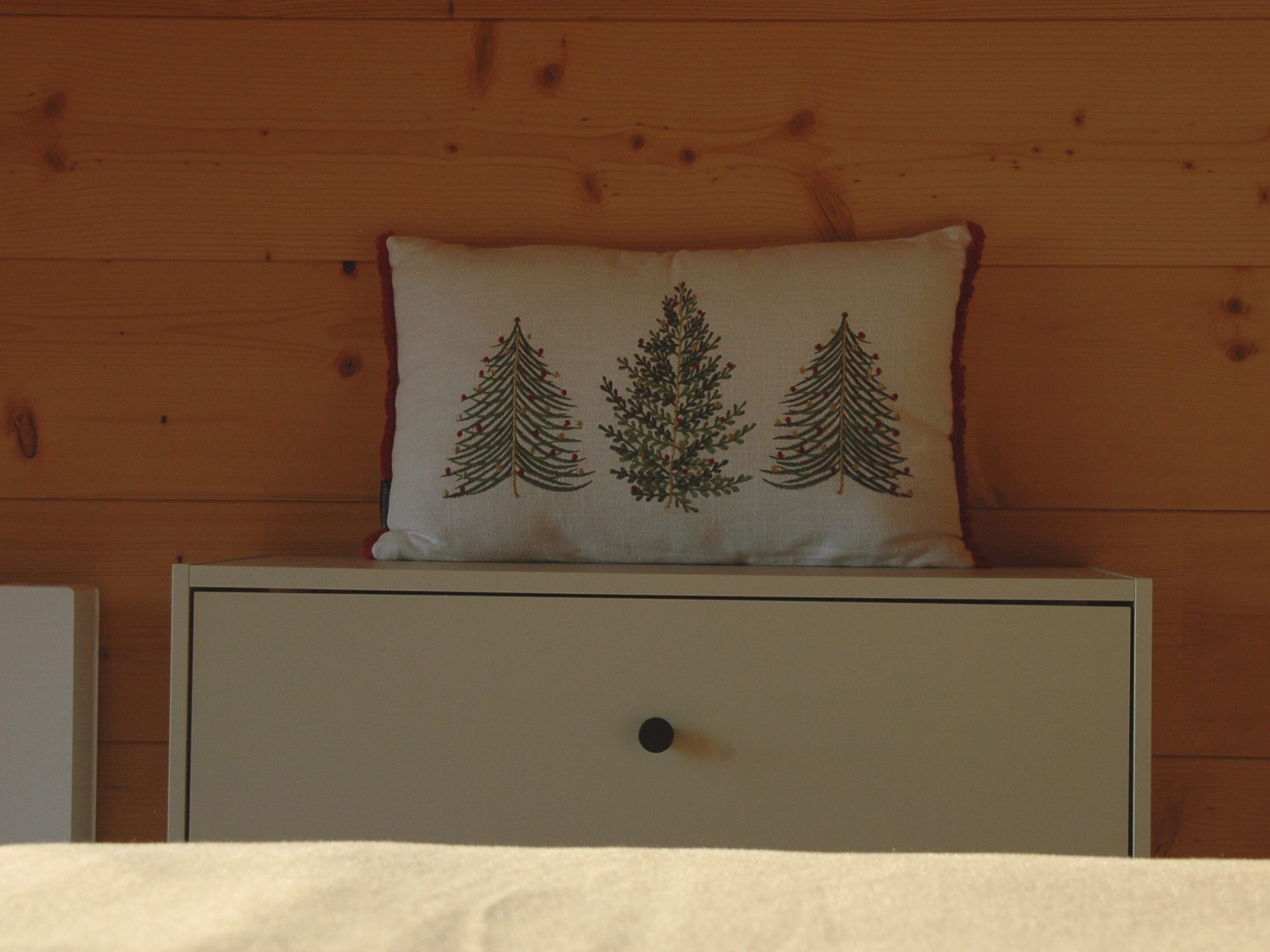 Chambre double de l'étage du chalet La Godille, location en Savoie. Détail sur un coussin avec des sapins brodés.